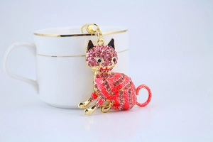 Detail of pink rhinestone lucky cat keychain next to a luxury white and gold cup