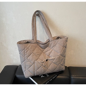 Detail of quilted tote bag with front pocket and double handles on a black stool