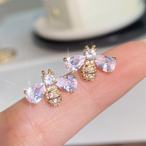 Macro detail of gold bee stud earring with pear-cut zircon held on a finger for scale