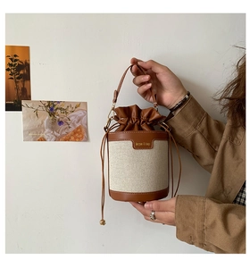 Detail of canvas bucket bag with brown leather trim and drawstring closure