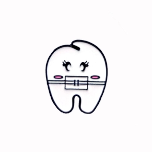 Dettaglio di una graziosa spilla a forma di dente smaltata con guance rosa e contorni neri