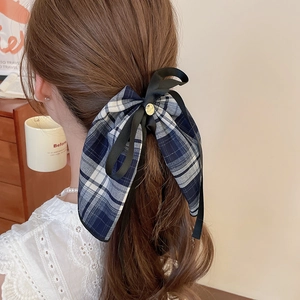 Detail view of a large blue and white plaid bow hair tie worn on a ponytail