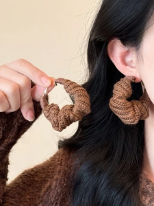 Détail de boucles d'oreilles créoles torsadées en tricot marron avec fermoir doré