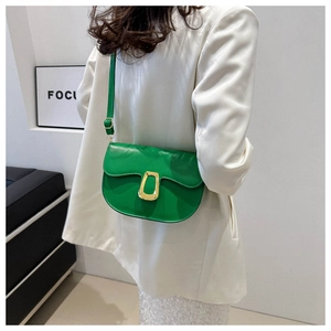 Detail of green saddle bag with gold trapezoid buckle worn over white blazer