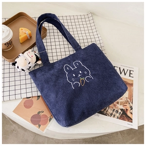 Detail view of navy blue corduroy tote bag featuring rabbit embroidery and cow plush charm