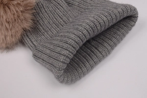 Gros plan d'un bonnet en tricot gris avec pompon en fausse fourrure beige et côtes