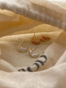 Detail of C-shaped triple-layered gold and silver stud earrings on beige linen bag