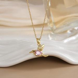 Macro detail of hummingbird pendant with pink heart stone and zirconia on gold chain