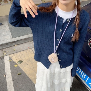 Close-up of navy blue cable-knit cardigan with white logo and a beige plush mini bag