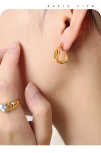 Close-up of elegant gold irregular curved earrings and heart-shaped zircon ring on model