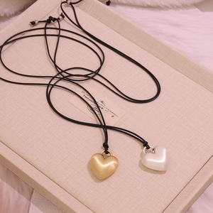Close-up of matte gold and pearl white heart pendants on black leather cords