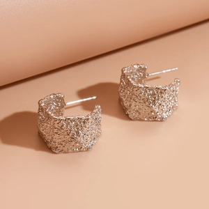 Macro view of C-shaped silver earrings featuring unique textured hammered finish