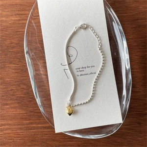 Detail of silver snake chain and gold beaded bracelet with heart pendant on display