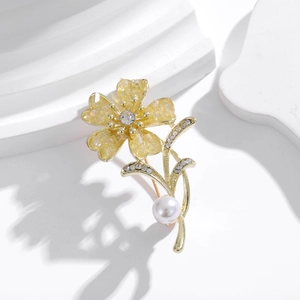Detailed shot of a gold floral brooch with yellow petals, clear rhinestones and a white pearl