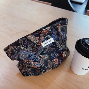 Close-up of vintage floral brocade cosmetic bag on wooden table with a coffee cup