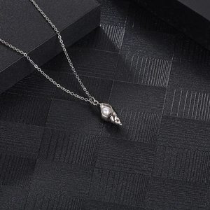 Macro detail of silver conch pendant with an inlaid white pearl on a black display pad