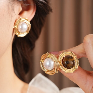 Close-up of golden pearl and tiger eye stone earrings with vintage twisted texture