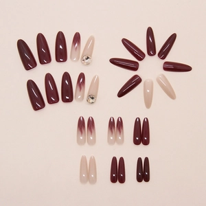 Close-up of long almond press-on nails with burgundy marble effect and small rhinestones