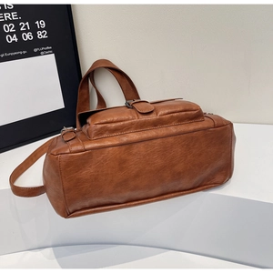 Detail view of brown vintage PU leather tote bag texture and buckle strap on white stand