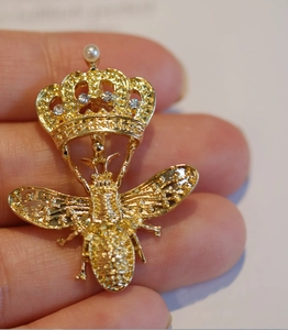 Broche abeille dorée tendance avec strass et couronne de perles sur le doigt