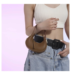 Close-up of brown lychee leather crescent bag with gold hardware and tassel detail