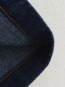 Gros plan du tissu denim bleu foncé avec des surpiqûres orange détaillées sur le bord