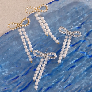 Flat lay of bow-knot pearl drop earrings in gold and silver over blue glass