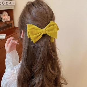 Model wearing large yellow flocked velvet bow hair clip with a cozy lifestyle backdrop