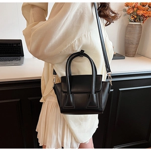 Model wearing black matte leather bucket bag with gold hardware in home office setting