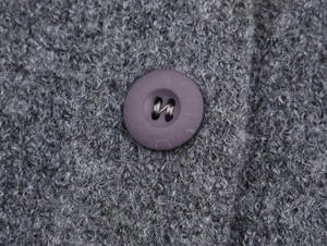 Macro detail of soft grey knit fabric with a purple button on a warm plush cardigan