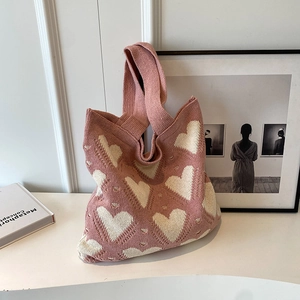 Pink knitted tote bag with white heart patterns shown in a lifestyle setting