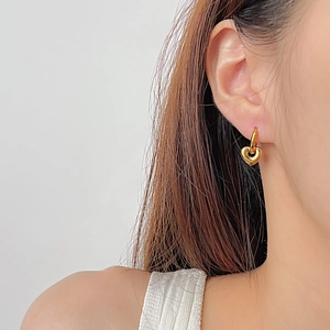 Close-up of a gold heart dangle earring worn by a model to show size and fit