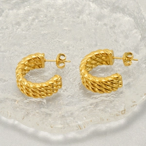 Detailed view of golden twisted hoop earrings on glass tray with silk fabric backdrop