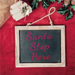 Detail of wooden Santa Stop Here hanging sign on red velvet background with decor