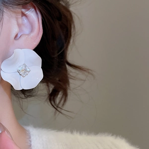 Close-up of white 3D flower earring with a square crystal centerpiece on model