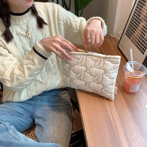 Detailed view of cream quilted clutch featuring artistic animal patterns on a wooden table