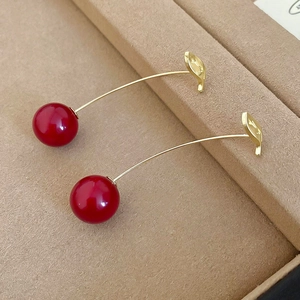 Macro shot of elegant red resin cherry earrings with golden leaves on leather jewelry box