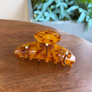 Detailed view of tortoiseshell resin hair claw with rhinestone-studded metal bows