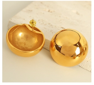 Macro shot of minimalist gold spherical stud earrings on a natural stone surface