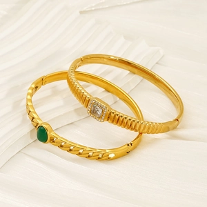 Detail of gold-plated bracelets featuring green gemstone and white zircon on white fabric