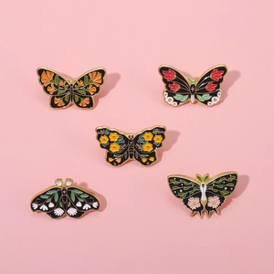 Detailed macro view of five vintage butterfly enamel pins with floral patterns on pink background