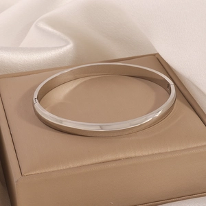 Silver stainless steel hinged bangle resting on beige gift box and white silk fabric