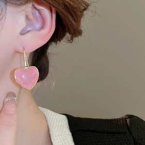 Close-up of sweet pink resin heart earrings with gold metal hooks on female model