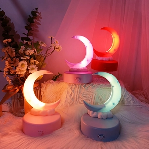 Detail of four moon-shaped night lights in pink, red, blue, and yellow on round bases