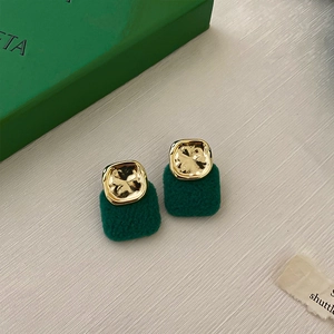 Detail of green flocked and gold square geometric stud earrings on a textured surface