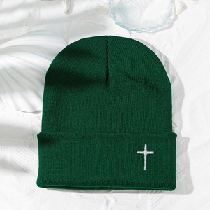 Détail du bonnet en tricot vert foncé avec broderie croix blanche sur fond de coquillages