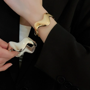 Detailed close-up of wavy gold and silver minimalist cuffs on a black fabric backdrop