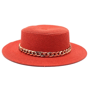Detail of red boater straw hat featuring a thick gold metal chain band and fine texture