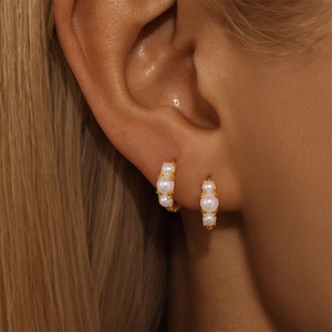 Macro detail of gold huggie hoop earrings featuring three small pearls on the ear