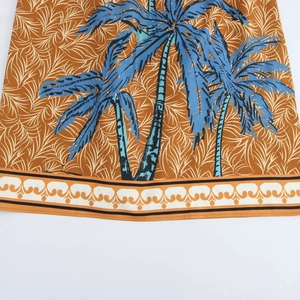 Brown resort dress featuring blue coconut tree prints and a wavy border hem detail